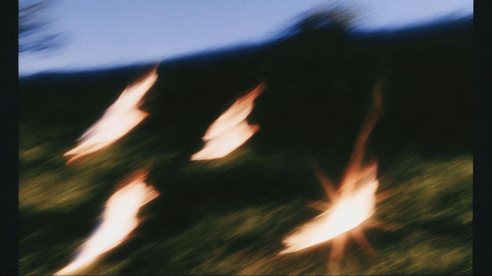 Three figures of warm light moving across a hillside